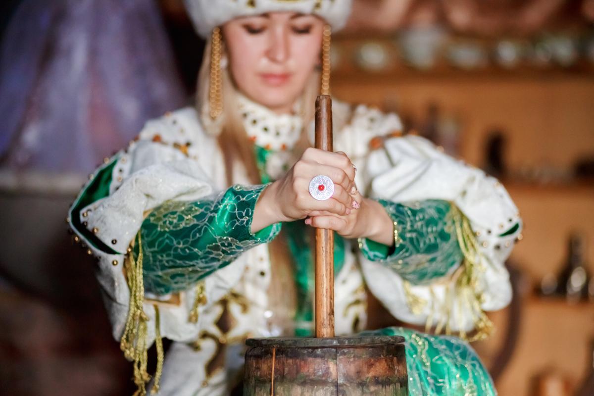 Молодая женщина в традиционном костюме взбивает масло